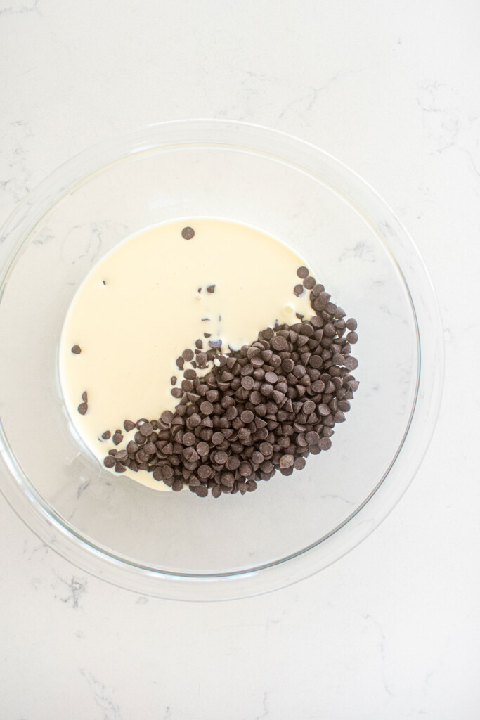cream and dark chocolate in a glass mixing bowl on a marble counter.