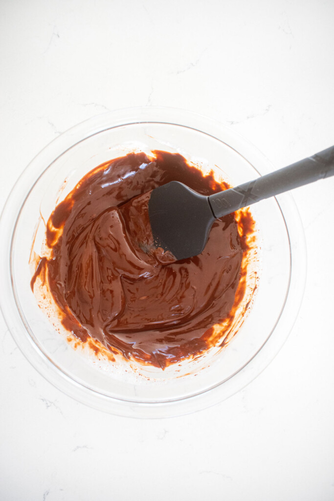 dark chocolate ganache in a glass mixing bowl on a marble counter.