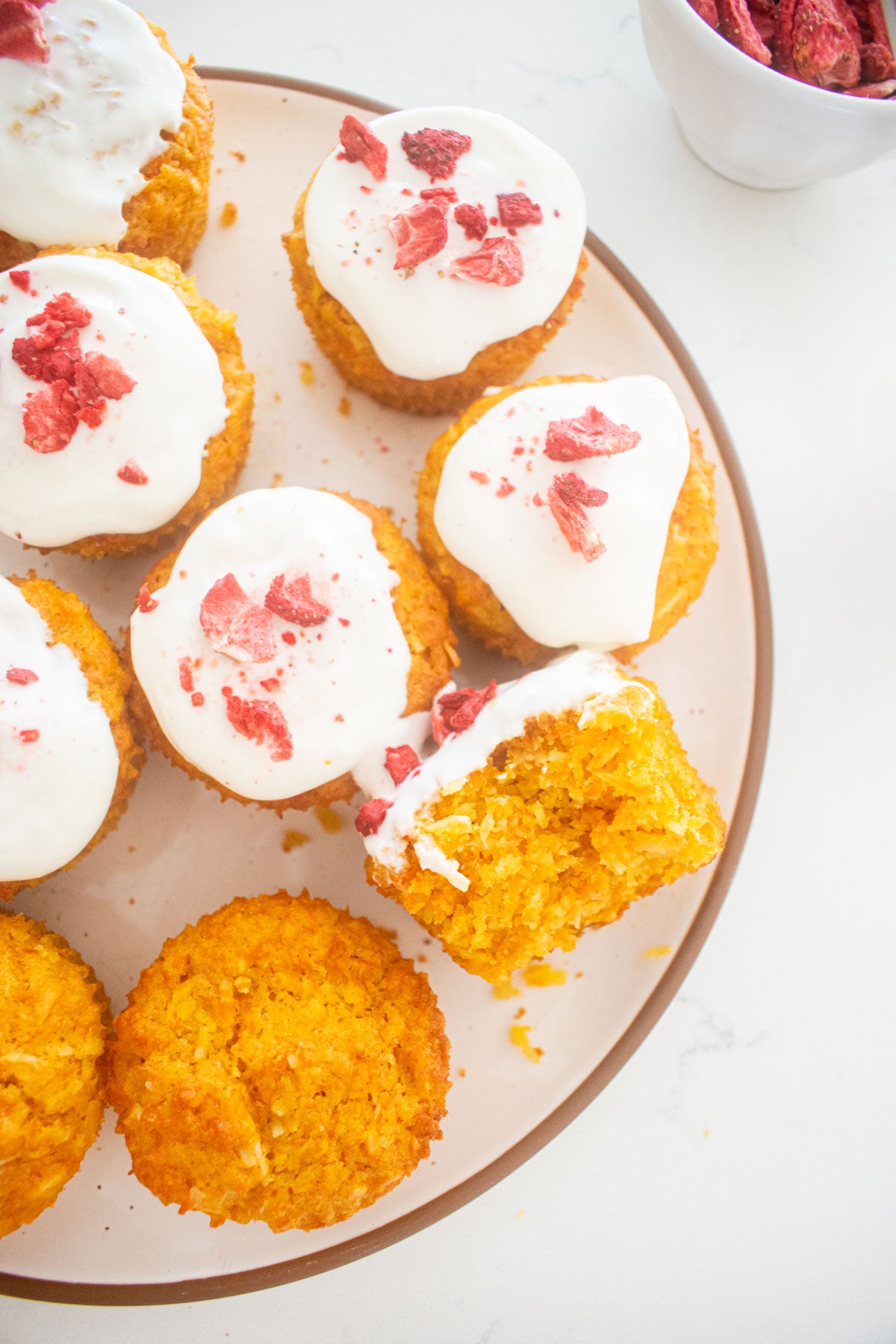 homemade pupcakes frosted with greek yogurt and strawberries on a plate, one with a bite taken out of it.