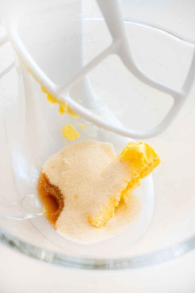 butter, sugar and vanilla in a glass mixing bowl on a marble counter.