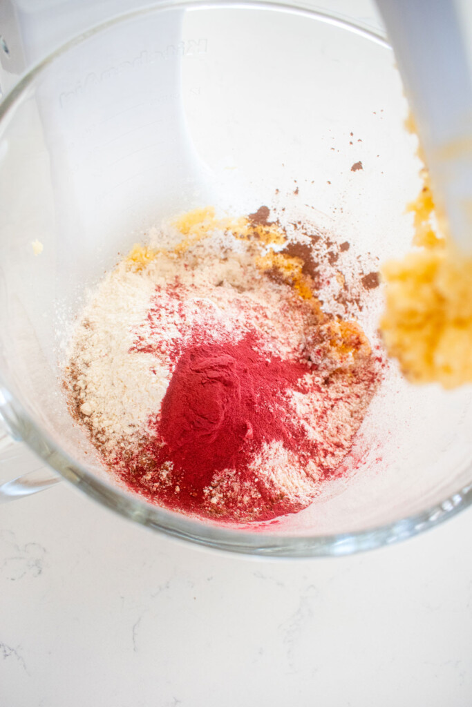 ingredients for sourdough red velvet cookies in a glass mixing bowl on a marble counter.