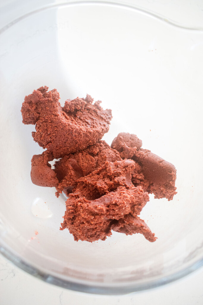 red velvet cookie dough without food coloring in a glass mixing bowl on a marble counter.