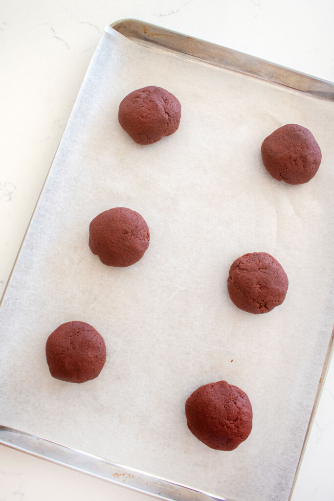 sourdough red velvet cookie dough balls on a baking sheet on a marble counter.