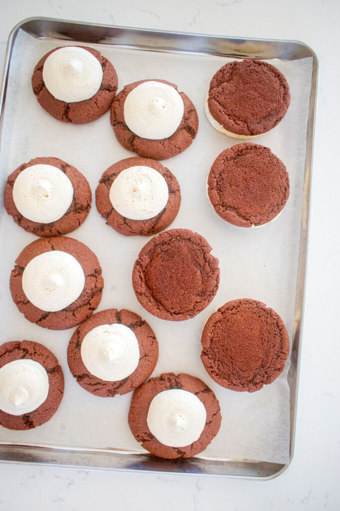 sourdough red velvet cookies without food coloring topped with cream cheese frosting on a baking sheet, with some turned over.