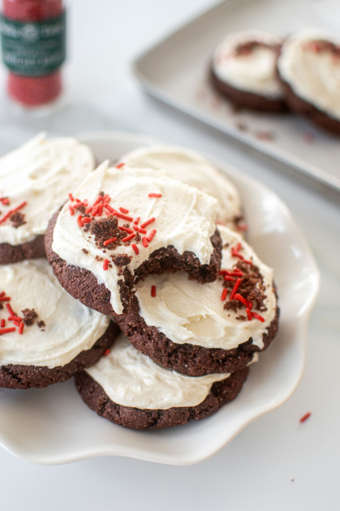 sourdough red velvet cookies with cream cheese frosting and red sprinkles on a plate on a marble counter.