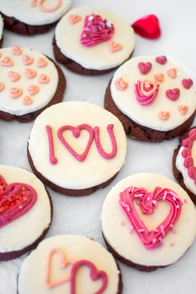 sourdough red velvet cookies with cream cheese frosting and valentine's day buttercream decor on a baking sheet on a marble counter.