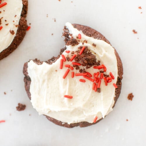 sourdough red velvet cookie with cream cheese frosting and red sprinkles on a baking sheet.