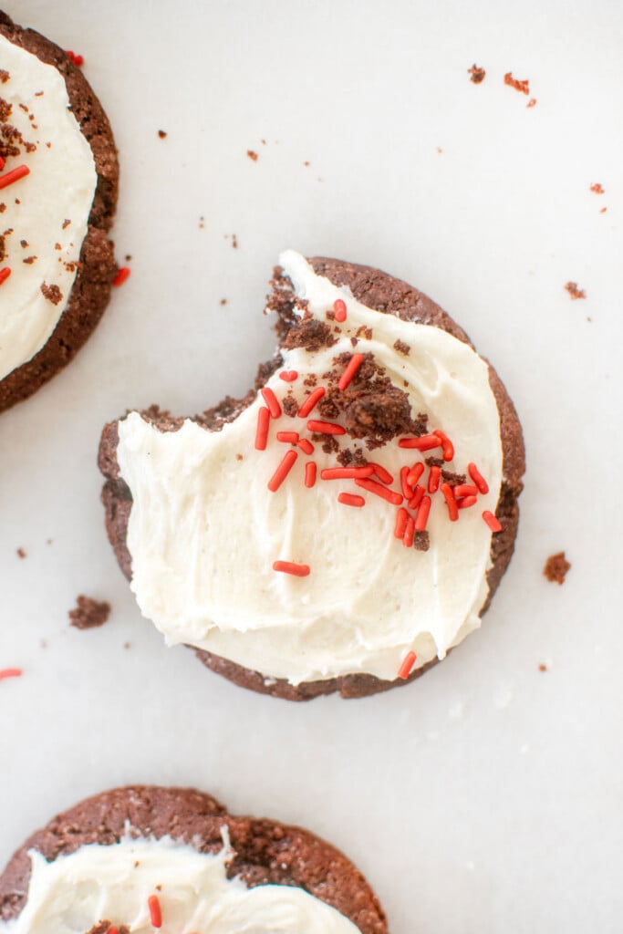 sourdough red velvet cookie with cream cheese frosting and red sprinkles on a baking sheet.