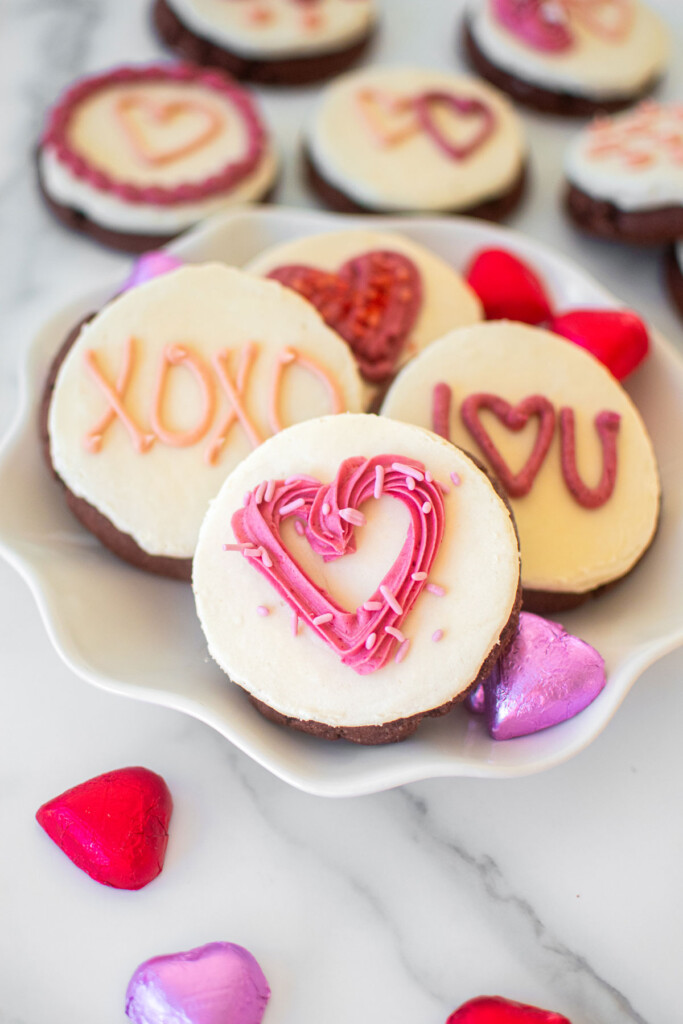 sourdough red velvet cookies with cream cheese frosting and decorated with valentine's day decorations on a plate on a marble counter.