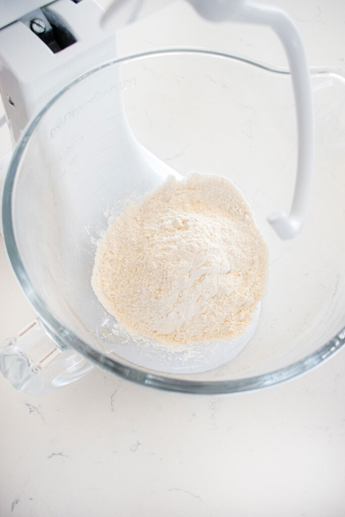 bread flour in a glass mixing bowl on a white marble countertop.