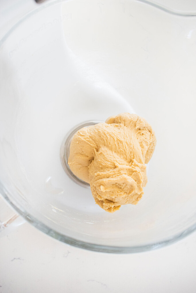 sourdough hot dog pretzel bun dough in a glass mixing bowl on a white marble countertop.