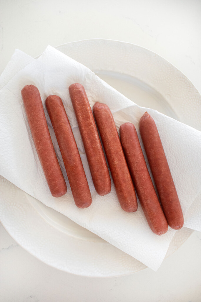 hot dogs on top of paper towels on a plate on a white marble countertop.