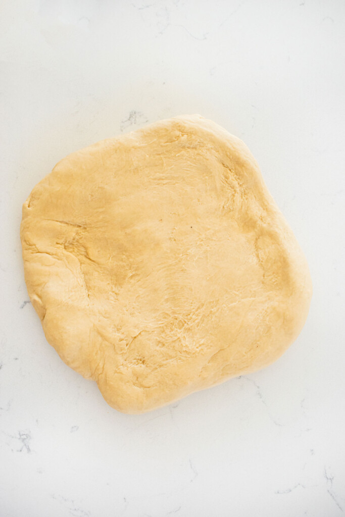 sourdough hot dog pretzel bun dough in a square on a marble countertop.