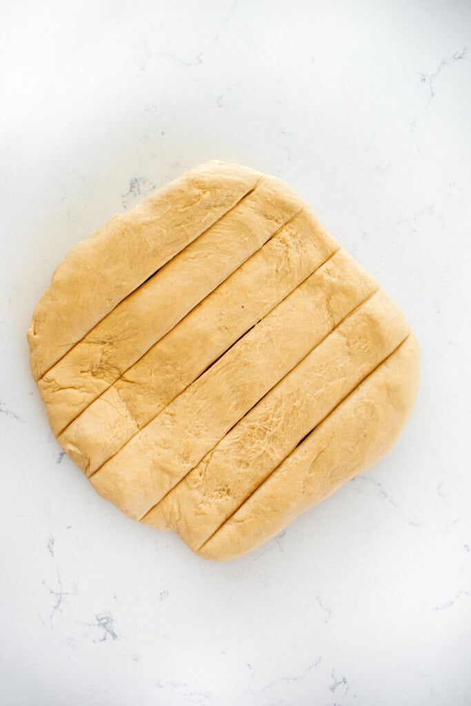 sourdough hot dog pretzel bun dough cut into strips in a square on a marble countertop.