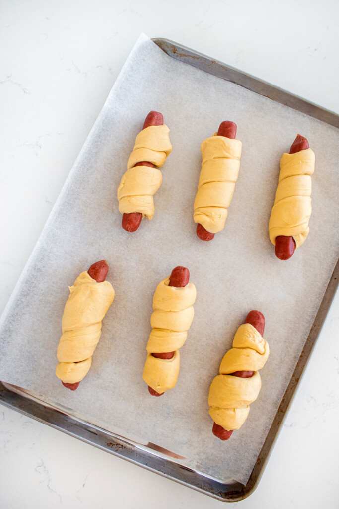 sourdough hot dog pretzel buns wrapped in hot dogs on a baking sheet on a marble countertop.