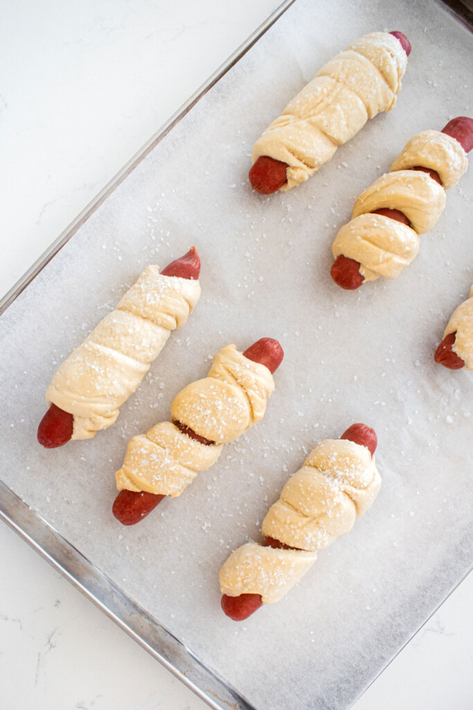 sourdough hot dog pretzel buns on a baking sheet on a marble countertop.