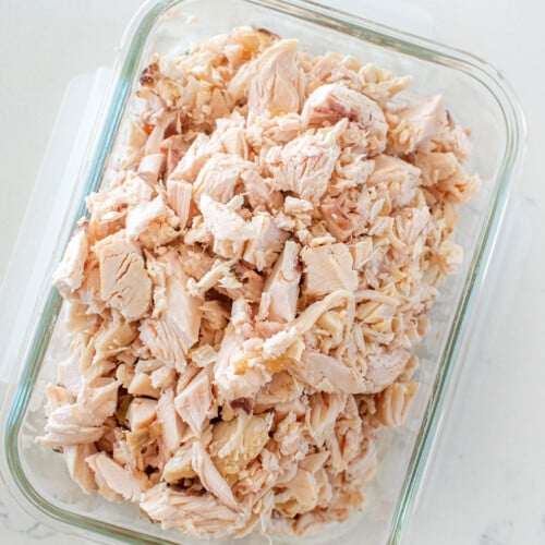 cooked chopped chicken in a glass tupperware on a white countertop.
