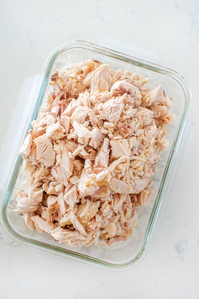 cooked chopped chicken in a glass tupperware on a white countertop.