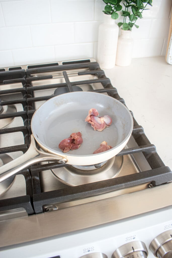 chicken giblets being cooked in a small frying pan on the stovetop.