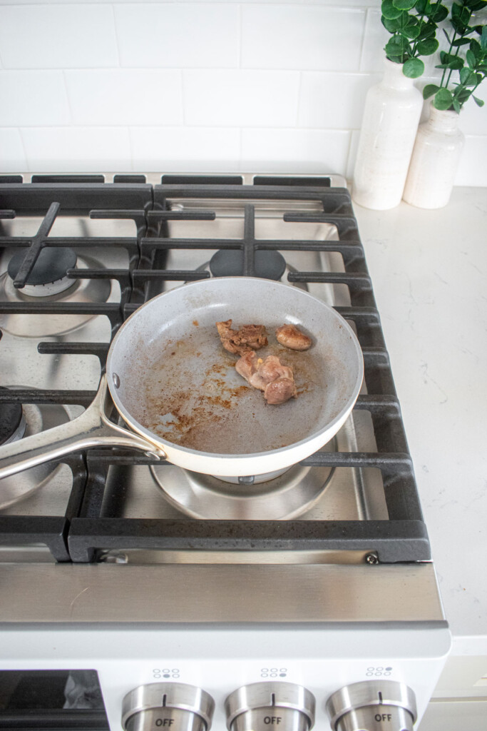 chicken giblets being cooked in a small frying pan on the stovetop.