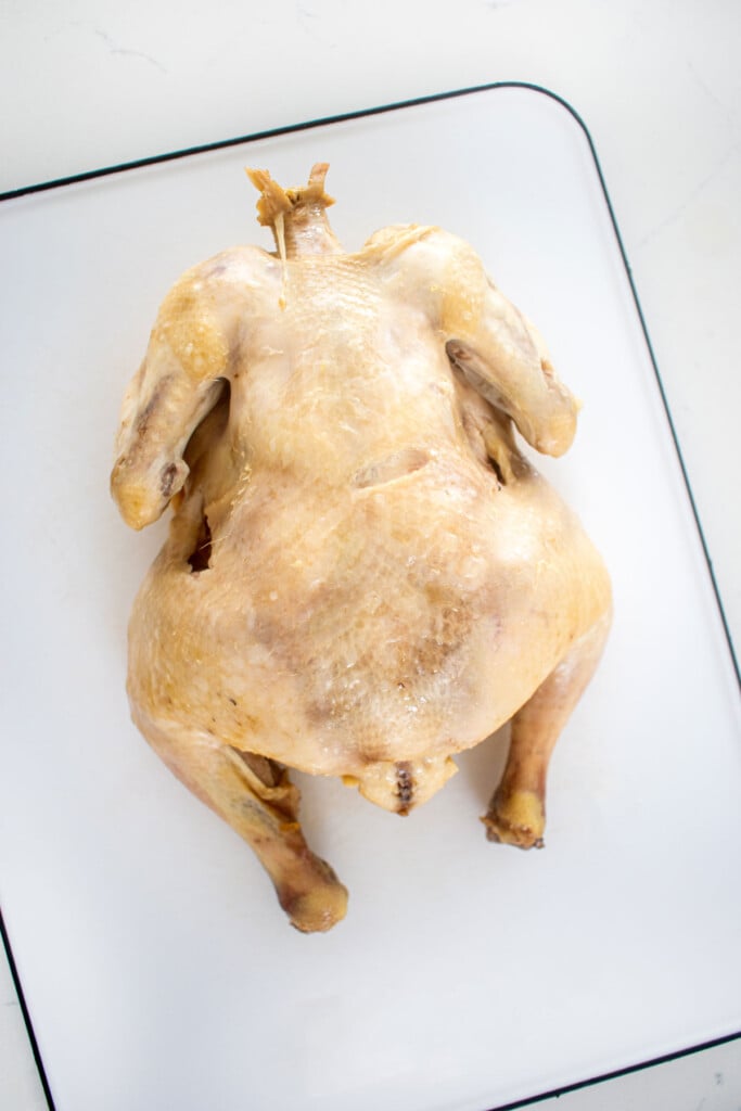 whole chicken on a cutting board on a white kitchen countertop.