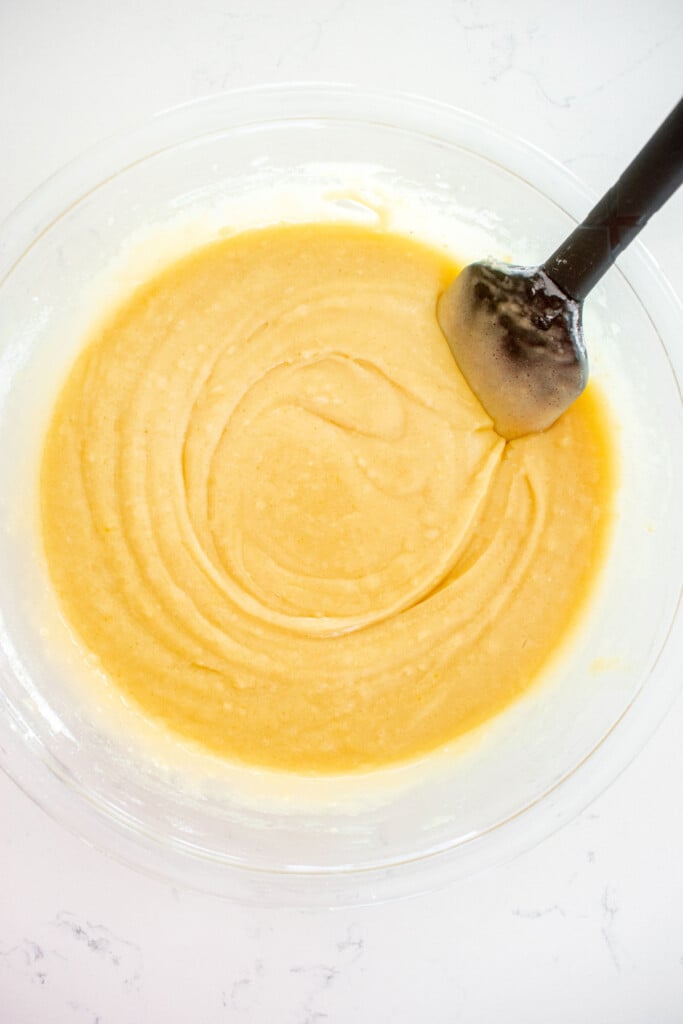 vanilla cake batter in a glass mixing bowl with a spatula on a white marble counter.