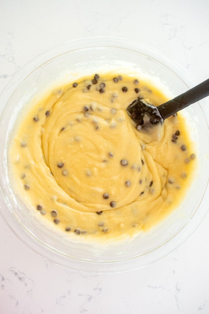 chocolate chip cookie dough cake batter in a glass mixing bowl with a spatula on a white marble counter.