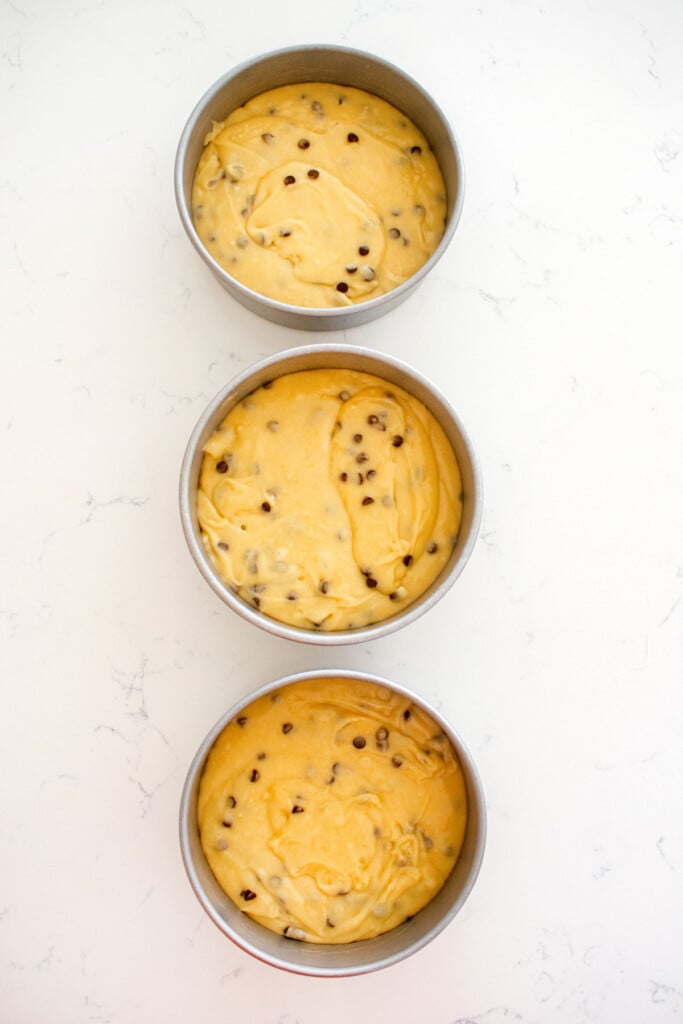 cookie dough cake batter in cake pans on a white marble counter.