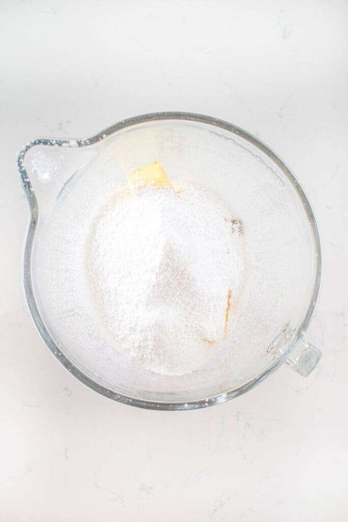 ingredients for cookie dough frosting in a glass mixing bowl on a white marble counter.