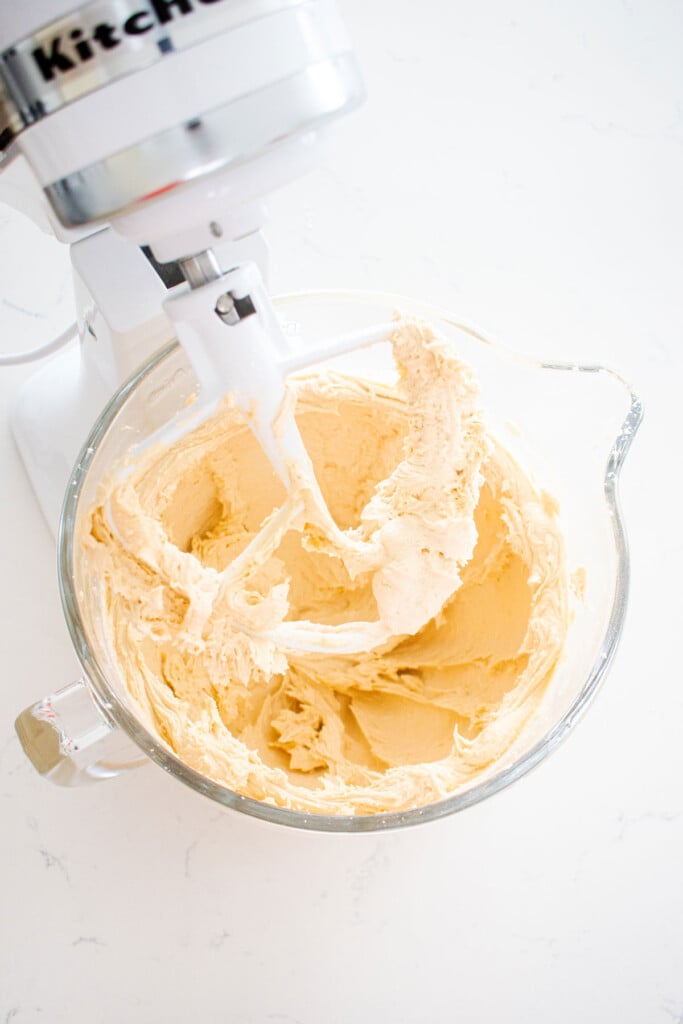cookie dough frosting mixed together in a glass mixing bowl on a white marble counter.