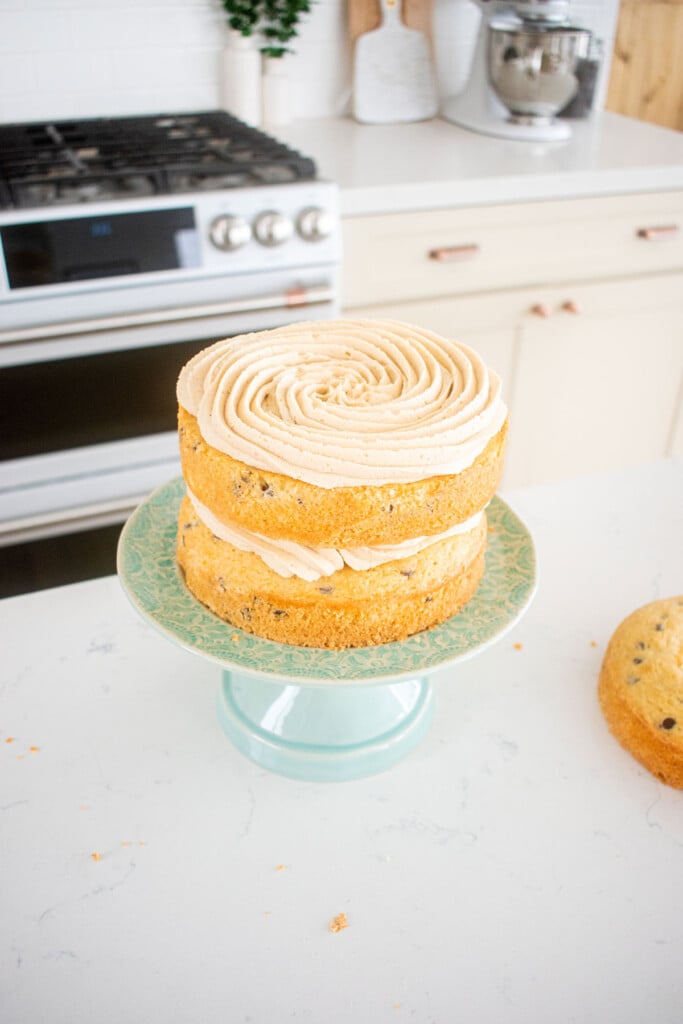 cookie dough layer cake being assembled on a green cake stand on the kitchen counter.