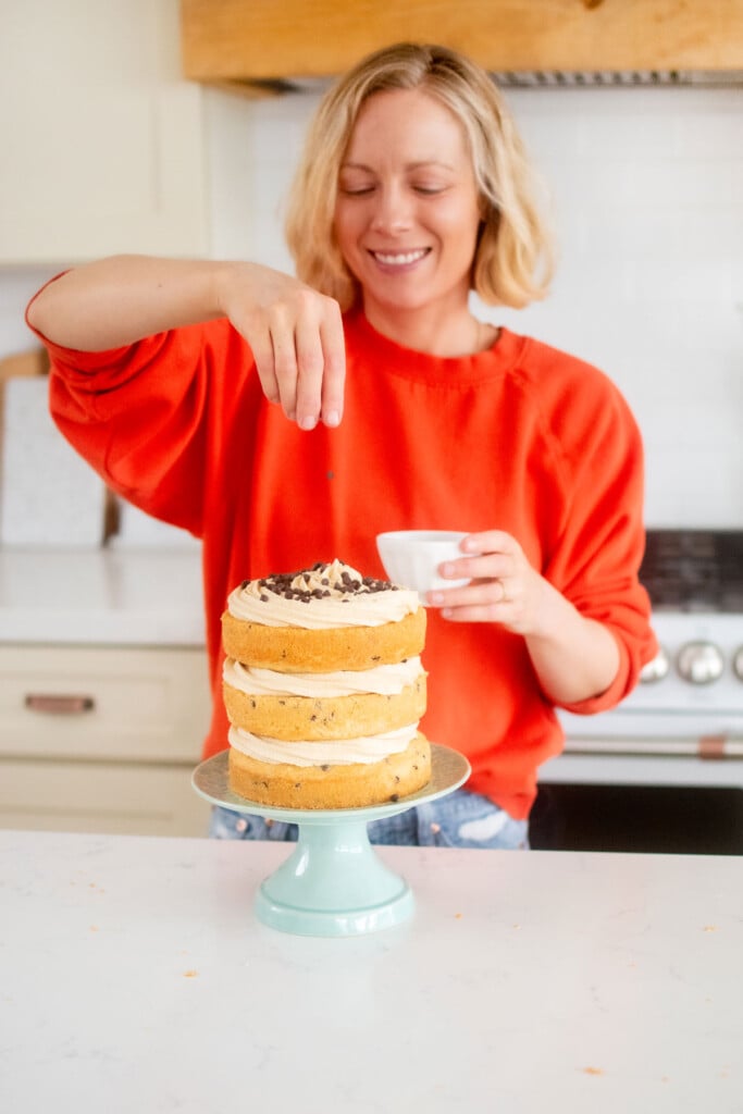 woman decorating cookie dough layer cake with mini chocolate chips at the kitchen counter.