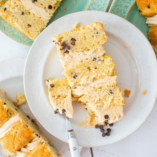 cookie dough layer cake on a cake plate with a fork on a white wood table.