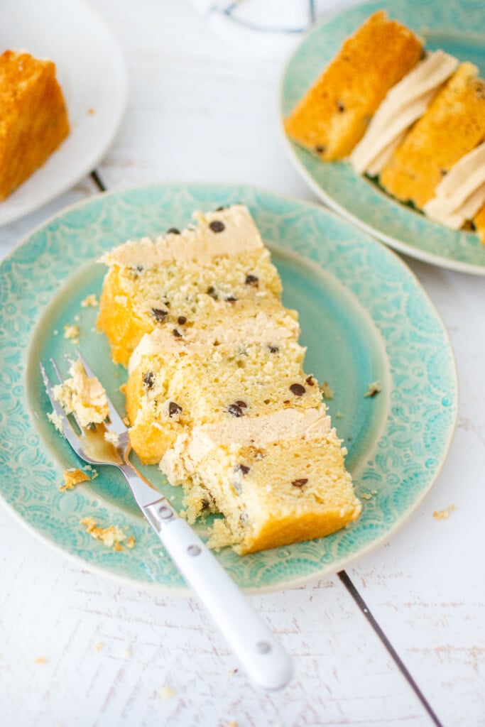 cookie dough layer cake on a cake plate with a fork on a white wood table.