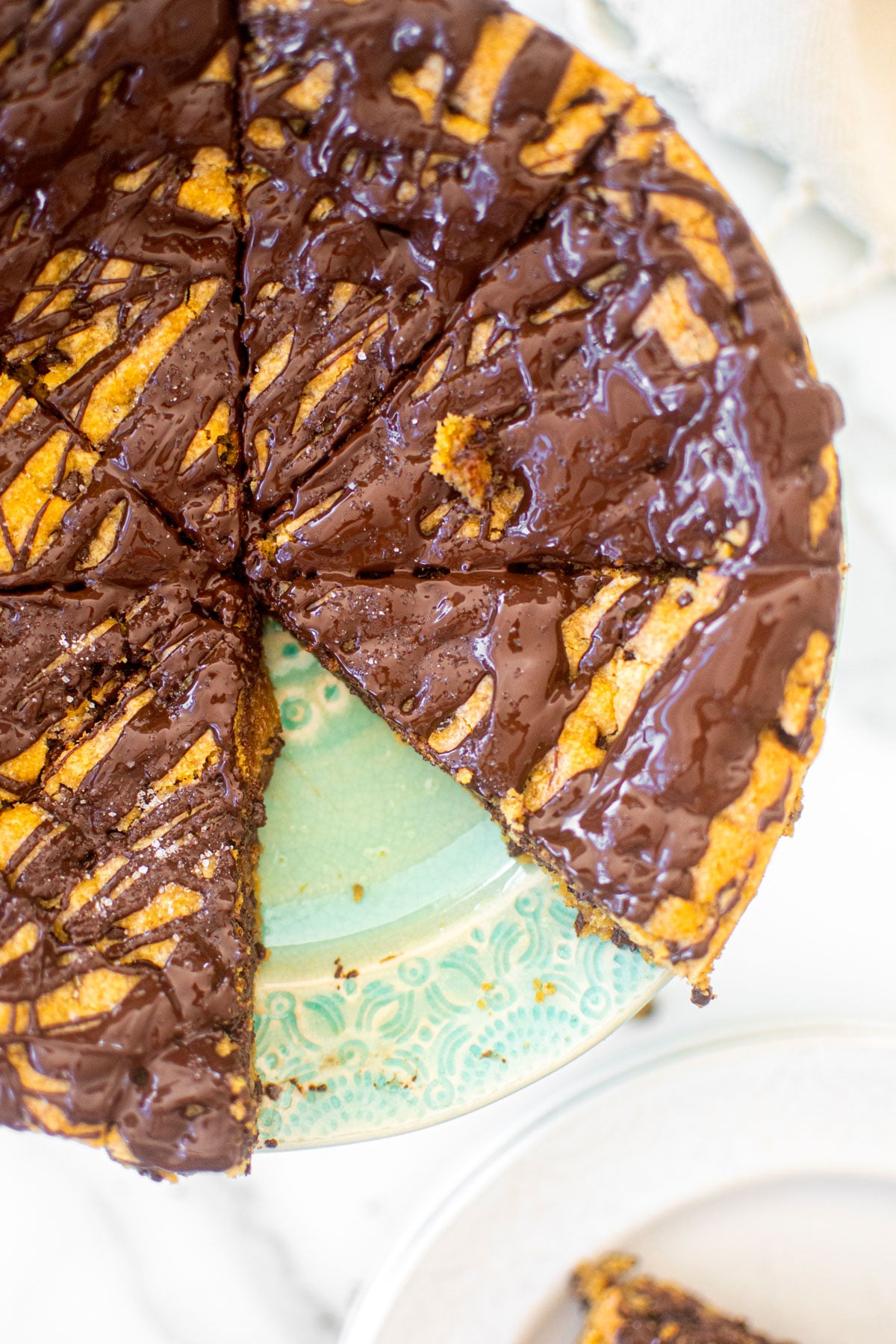 eggless chocolate chip cookie cake cut into slices on a green cake plate.