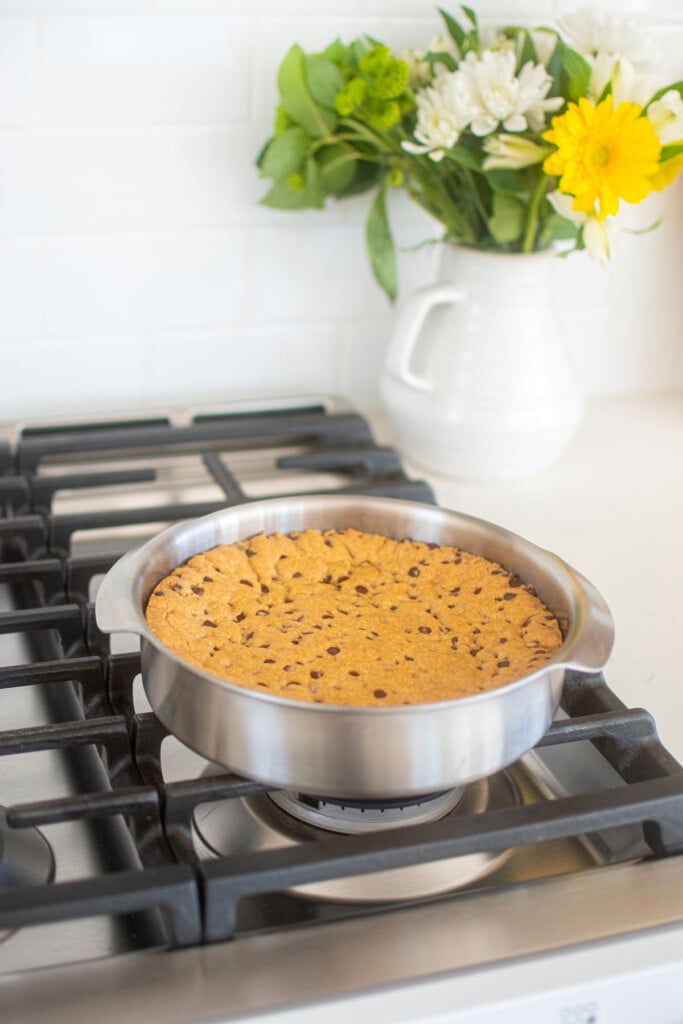 eggless chocolate chip cookie cake in a cake pan cooling on top of an oven.
