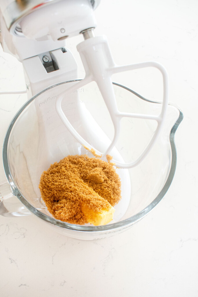 butter brown sugar and vanilla in a glass mixing bowl on a white marble counter.