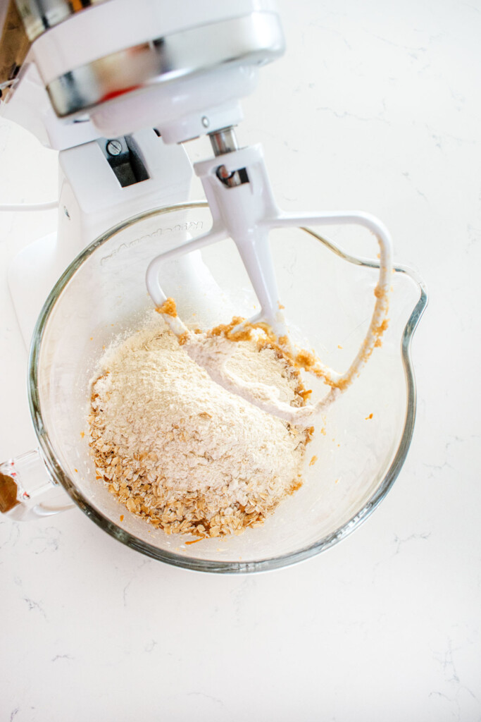 ingredients for eggless monster cookies in a glass mixing bowl on a marble counter.