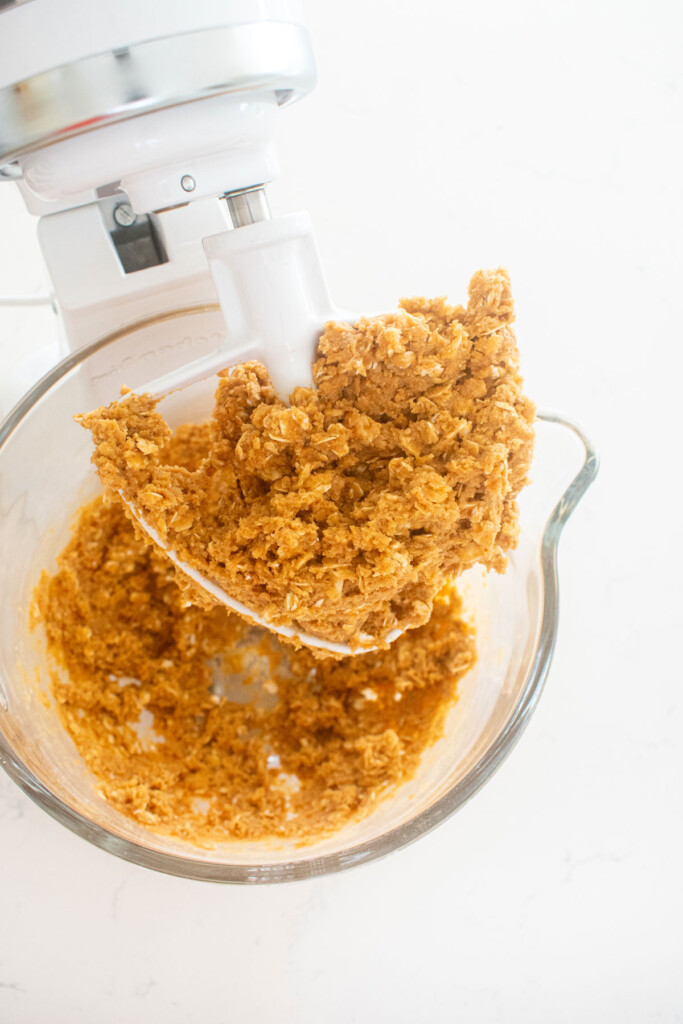 eggless monster cookie dough in a glass mixing bowl on a white marble counter.