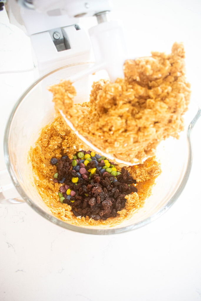 ingredients for eggless monster cookies in a glass mixing bowl on a marble counter.
