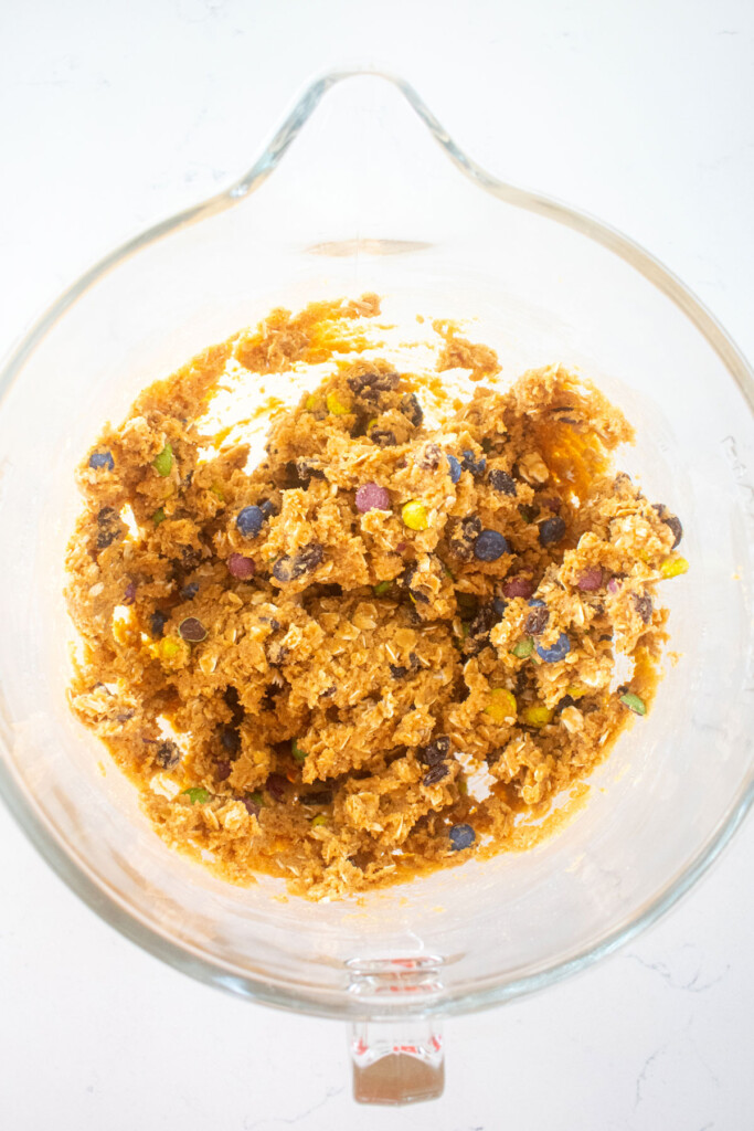 eggless monster cookie dough in a glass mixing bowl on a marble counter.