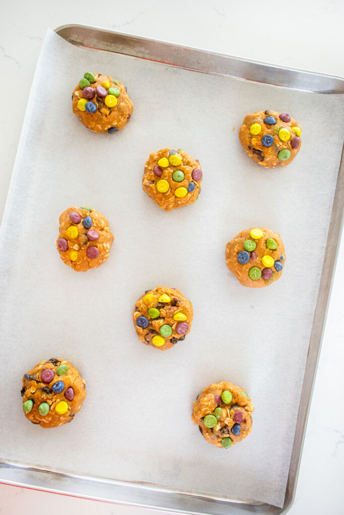 eggless monster cookie dough balls on a baking sheet on a white marble counter.