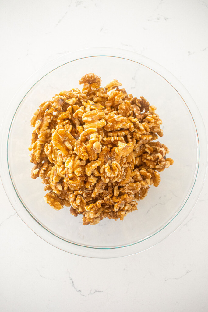 raw walnuts in a glass mixing bowl on a white marble countertop.