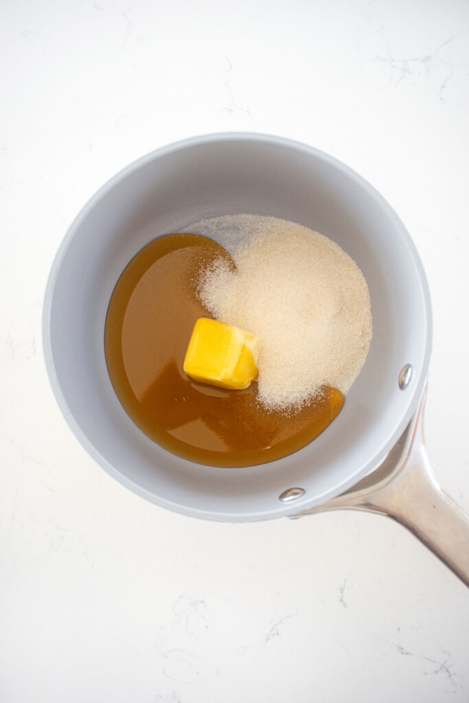 sugar, butter and hot honey in a small pot on a white marble countertop.