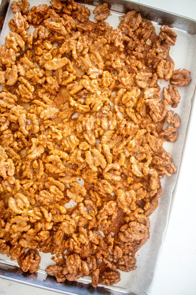 hot honey roasted walnuts on a baking sheet on a white marble countertop.