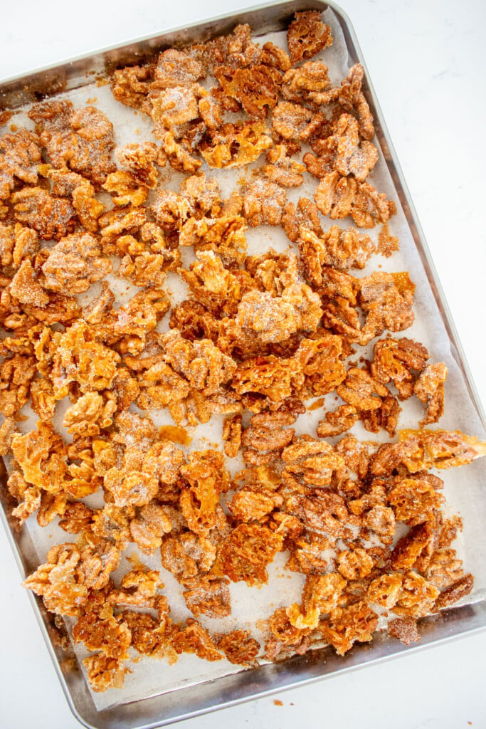 hot honey roasted walnuts on a baking sheet on a white marble countertop.