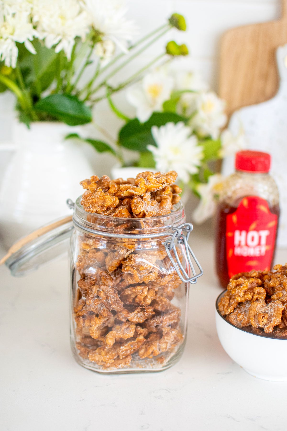 hot honey roasted walnuts in a glass jar on a white marble countertop.