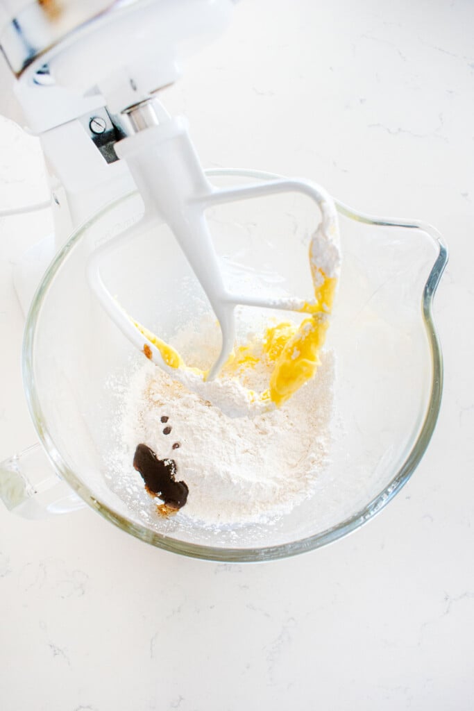 butter sugar and vanilla bean paste in a glass mixing bowl on a white marble counter.