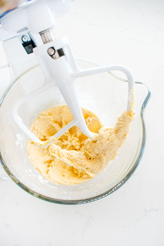 butter sugar and vanilla bean paste creamed together in a glass mixing bowl on a white marble counter.
