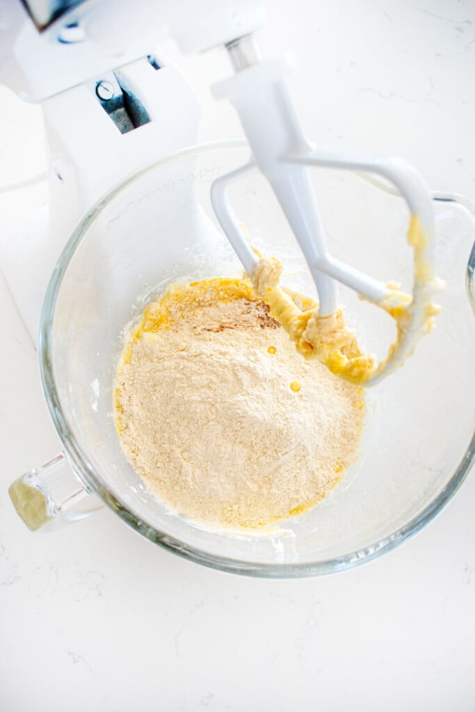 ingredients for sugar cookies in a glass mixing bowl on a white marble counter.